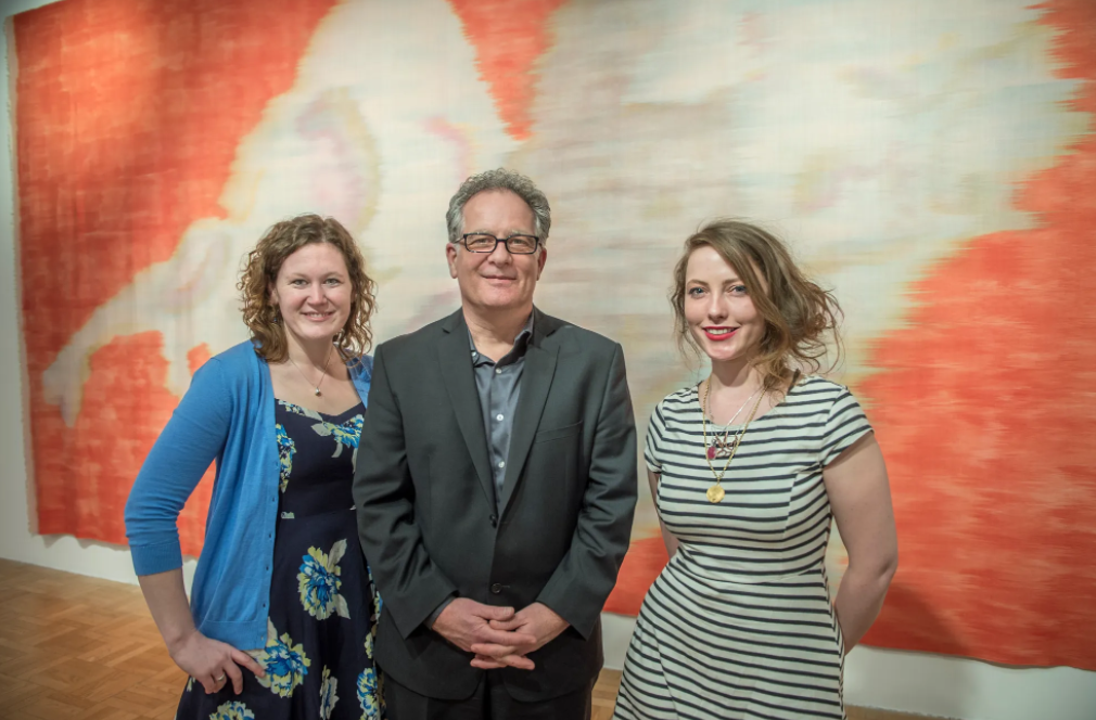 2 women and man smiling in front of silk artwork